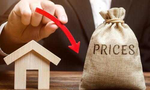 A bag with the word Prices, a miniature house and a down arrow in the hands of a businessman. The concept of reducing the market value of real estate. Low price for renting a house or apartment.