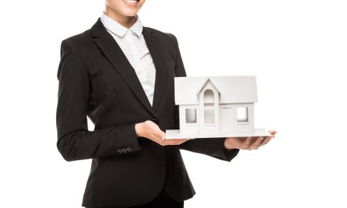 cropped shot of smiling young businesswoman holding miniature house model isolated on white