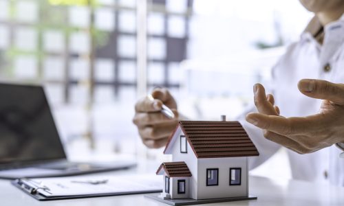 Home security and insurance concept - A close-up view of a man defending a home model by hand on a table in an office. And are explaining the agreement to the customer