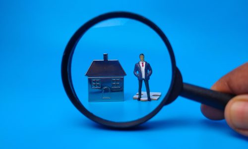 Miniature people,house keychain and magnifying glass on blue background. Real estate concept.
