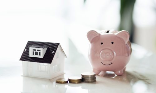 Pink piggy bank with tiny house on white marble background and blurred bokeh with copy space. Concept for financial home loan or money saving for house buying, real estate and insurance. High quality photo