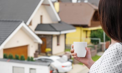 Young woman standing with a white cup in her hands and watching on the modern houses. Building of house of dream. Advertising concept for architecture company. Good neighborhood.